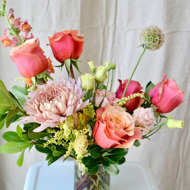 A vibrant arrangement with coral and red roses, a soft pink chrysanthemum, and accents of yellow and green. This cheerful bouquet is perfect for birthdays, congratulations, or to brighten someone's day. Available for local delivery in Wake Forest, NC.